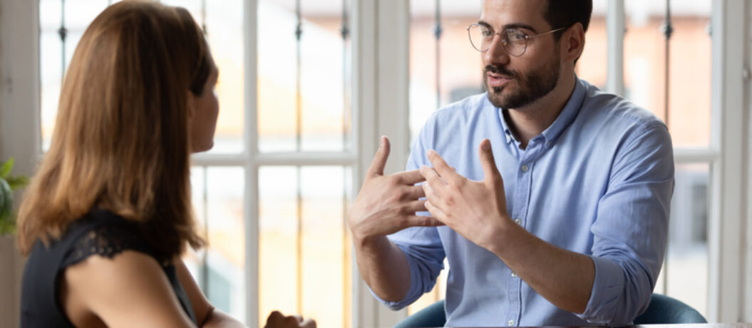 Confident male boss leader in eyeglasses explaining project details to new female employee at meeting. Concentrated young woman job applicant listening to hr manager questions at interview in office.