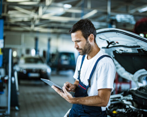 Young manual worker using touchpad while working in auto repair shop.